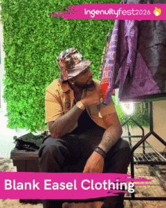 Blank Easel Clothing - IngenuityFest Vendor 2026 - Stylish man sitting next to a rack of shirts looking at a design.