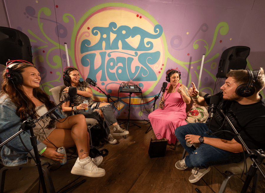 4 people in a recording studio talking laughing. Art Heals mural painted on the wall behind them.